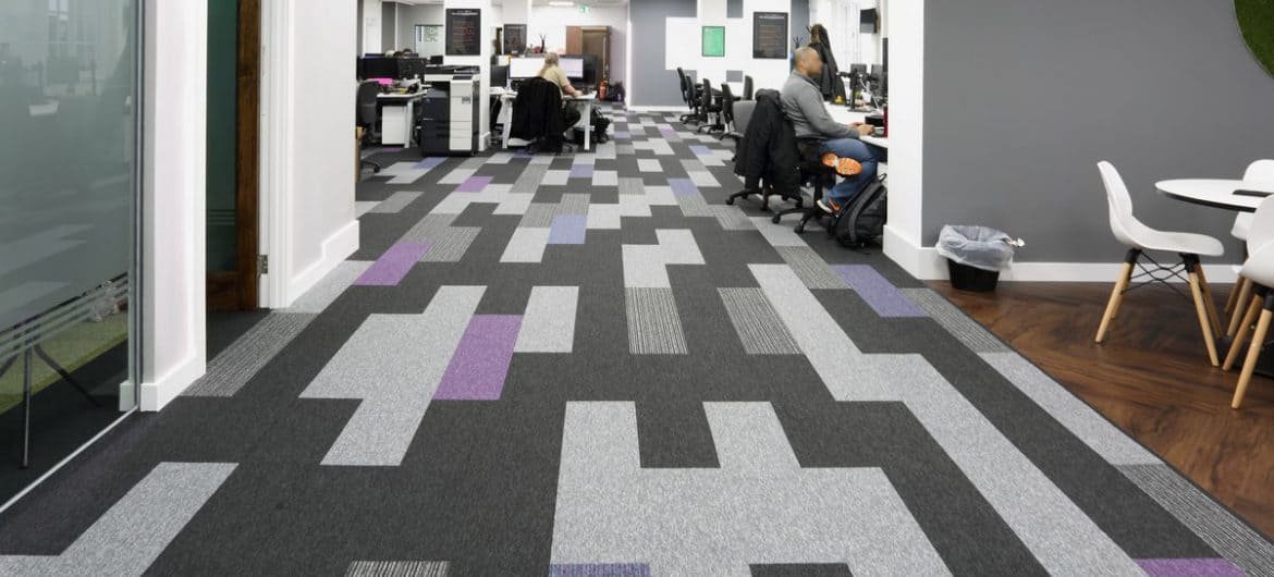 Espace de bureaux moderne en open-space à Saint-Jean-de-Luz équipé d'une moquette acoustique design à motifs géométriques gris anthracite, gris clair et touches violettes.